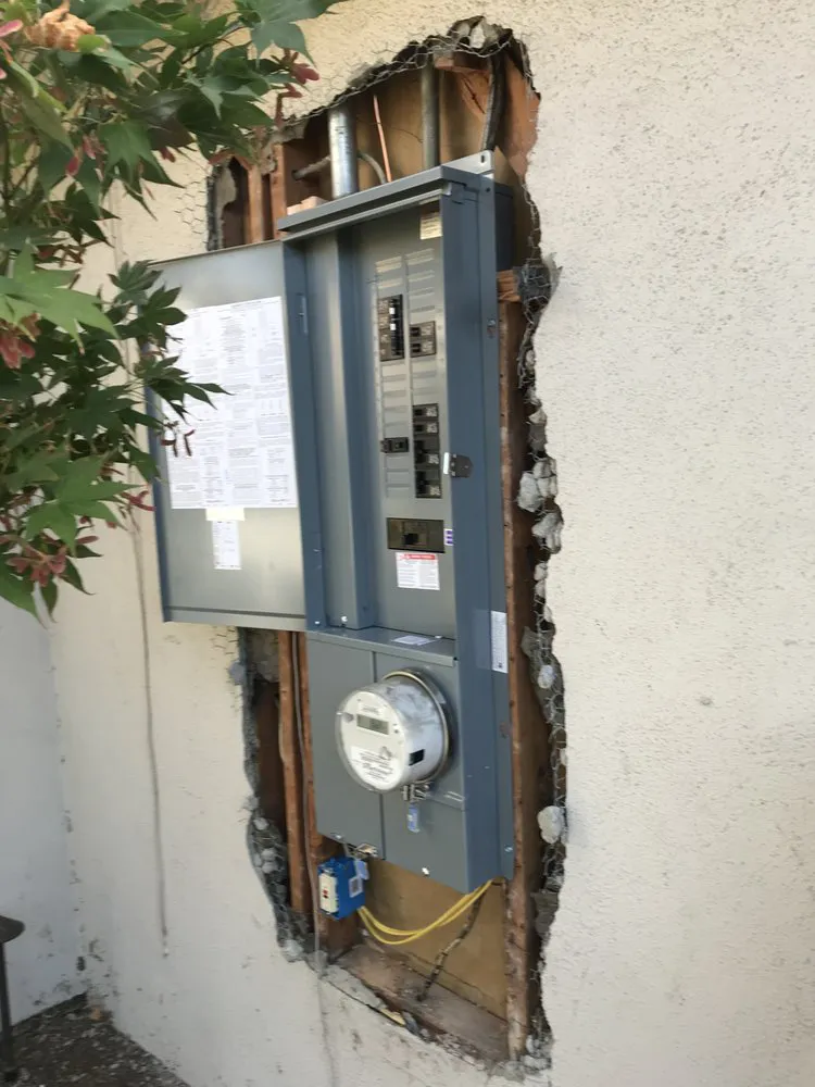An electrical panel on a wall, with visible wiring and a meter, installed by California Power and Light in Morgan Hill.