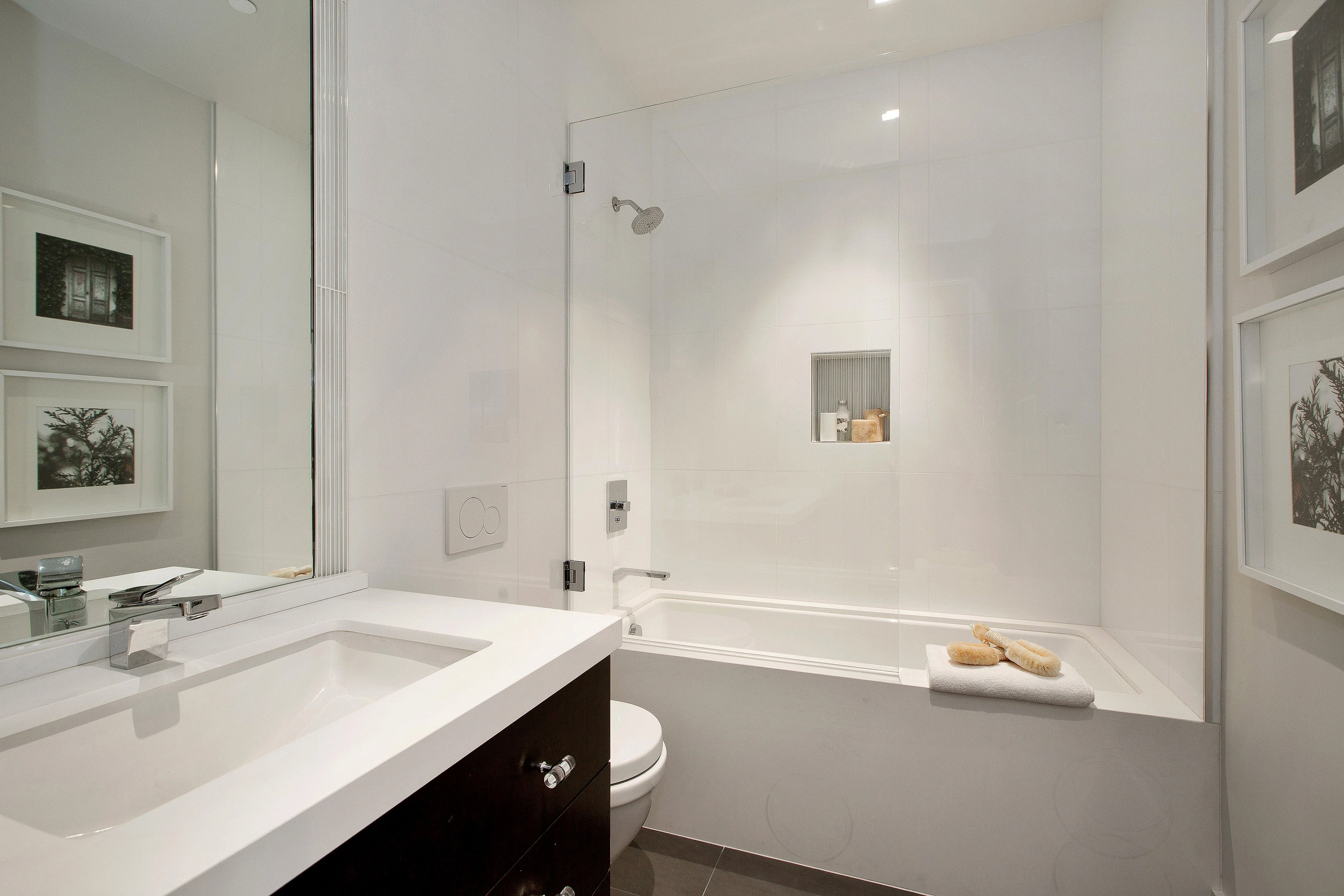 A modern bathroom featuring a glass shower door, white walls, a large mirror, and framed artwork, designed by California Shower Door Corporation in San Francisco.