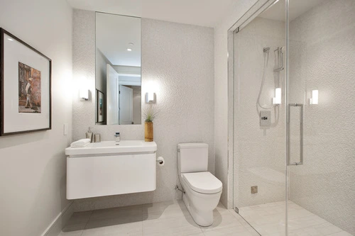 A modern bathroom featuring a glass-enclosed shower, wall-mounted sink, and toilet with minimalist decor.