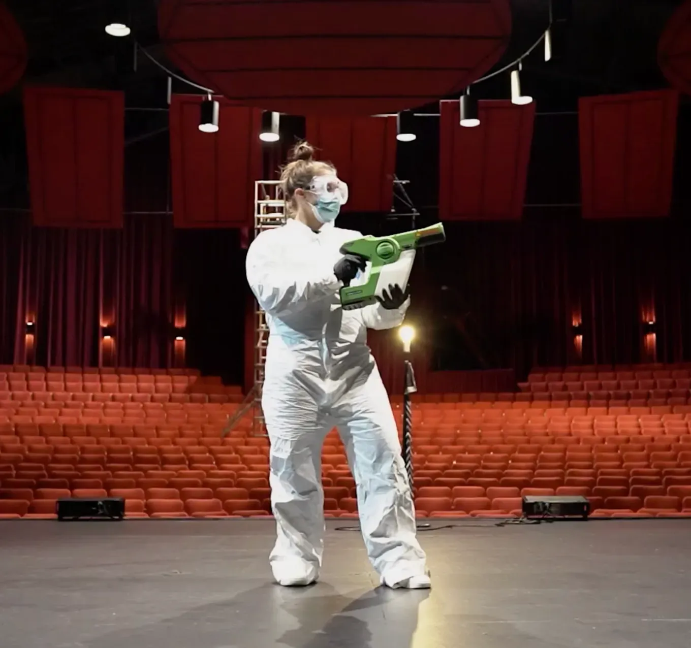 "A person in protective gear uses a fogging machine to disinfect an empty theater auditorium, highlighting Cappstone, Inc.'s commitment to hygiene in San Francisco."
