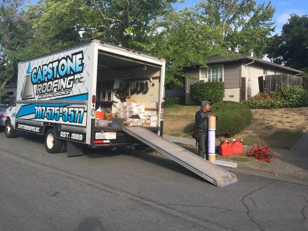 A Capstone Roofing, Inc. truck in Santa Rosa, parked by a house with an open back showing roofing materials and a worker nearby holding a roll of material.