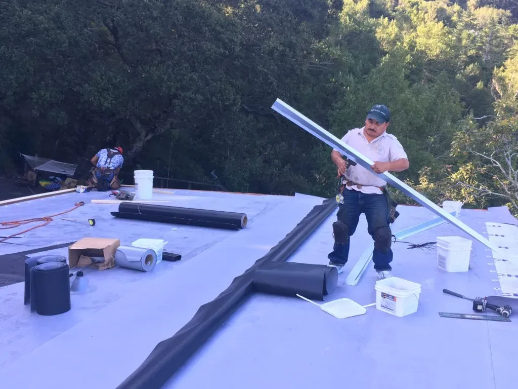 Two workers from Capstone Roofing, Inc. installing roofing materials on a flat roof, surrounded by lush greenery in Santa Rosa.