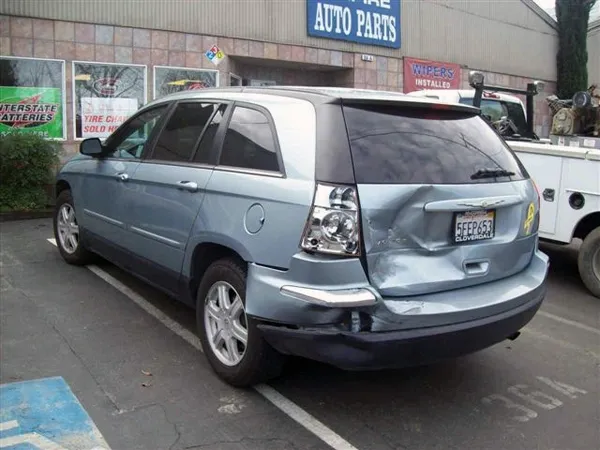 A damaged silver SUV with rear-end damage parked in front of an auto parts store.