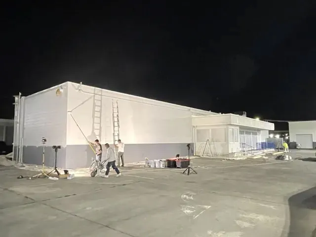 Night-time painting of a large commercial building by Cartwright Painters LLC in San Jose, featuring workers, ladders, and equipment.