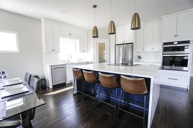 Modern kitchen featuring white cabinetry, a central island with seating, stainless steel appliances, and dark wood flooring, designed by Castles Home Service in Salinas.
