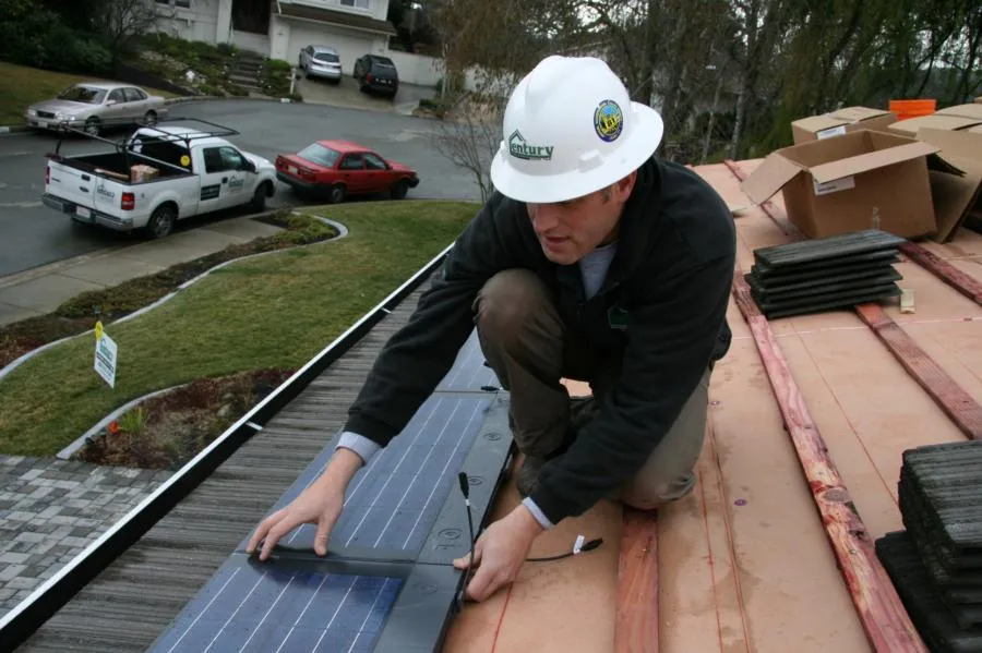 A worker from Century Roof and Solar installs a solar panel on a roof in Hayward, wearing a hard hat and uniform, with tools and materials nearby.