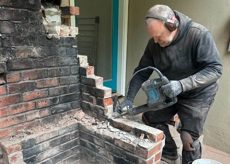 "A man wearing protective ear gear and gloves operates a power tool to repair a brick chimney, highlighting the expert service by Chimney Clean Company in San Jose."