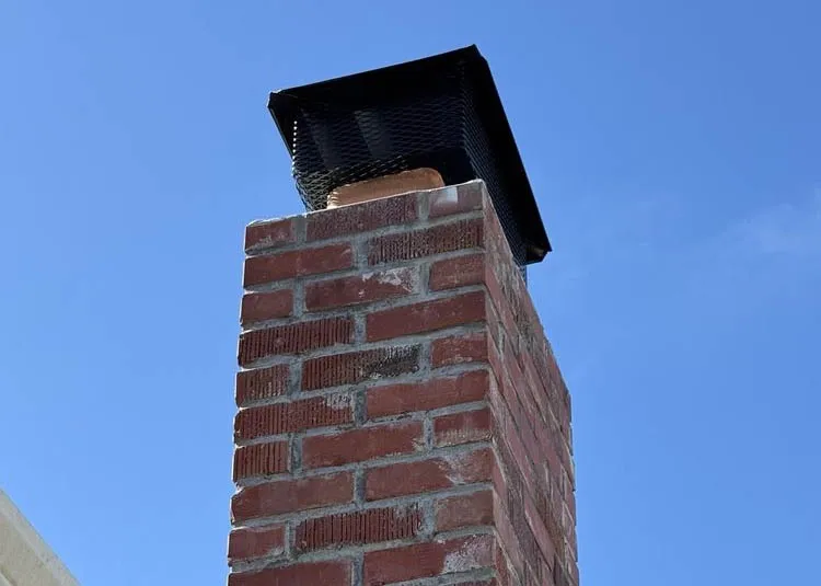 "A well-maintained brick chimney with a protective cap against a clear blue sky, serviced by Chimney Clean Company in San Jose."