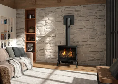 A cozy living room with a burning fireplace set against a stone wall, featuring a comfortable couch and shelves.