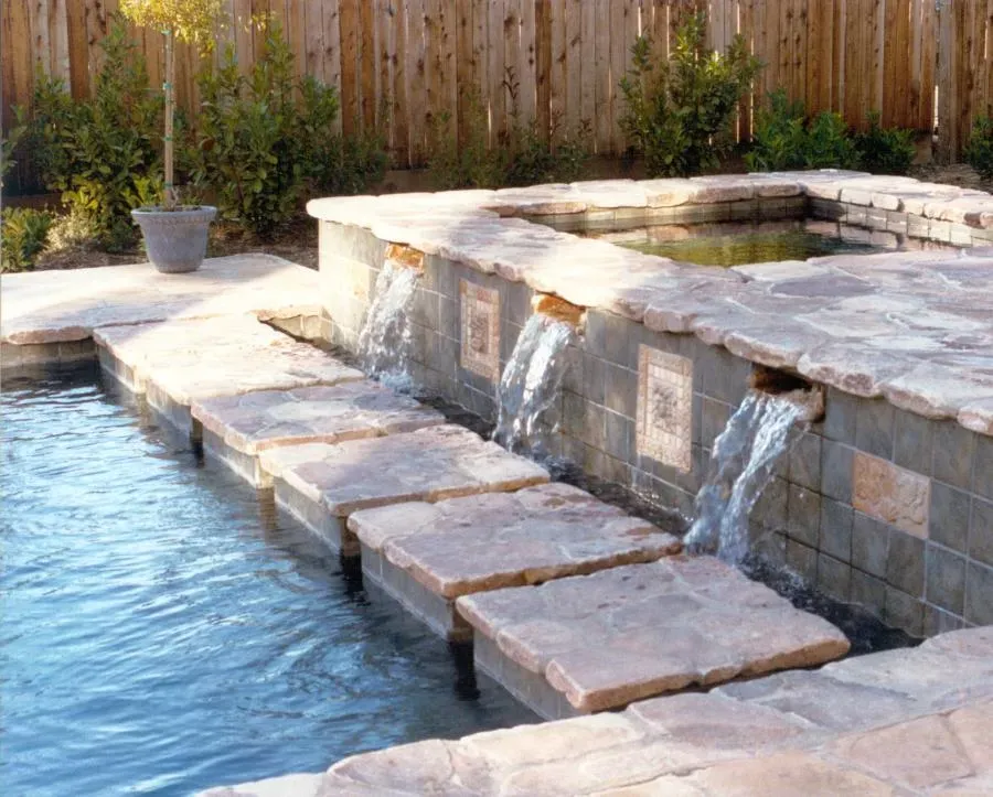 Outdoor pool water feature with stone slab bridge and cascading waterfalls, designed by Classic Pools in Concord.