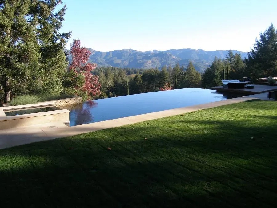 An infinity pool by Classic Pools in Concord, overlooking a scenic view of mountains and trees, with a green lawn surrounding it.