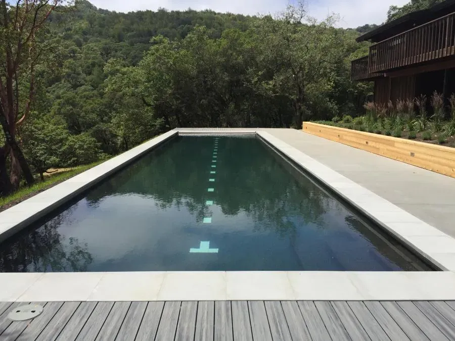 A rectangular lap pool surrounded by nature, with clear water reflecting the sky and a wooden deck adjacent to the pool, built by Classic Pools in Concord.