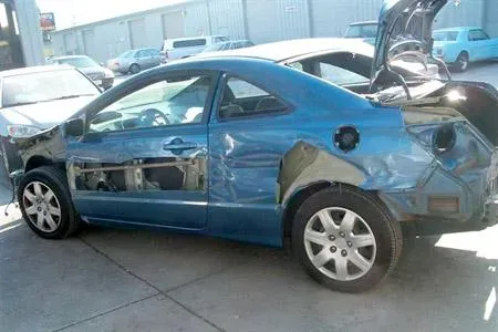 A damaged blue car with visible body damage is parked outside an auto repair facility at Coelho's Body Repair and Auto Sales in Fremont.