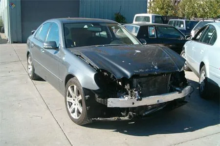 A damaged car with a missing front bumper and hood in need of repair at Coelho's Body Repair and Auto Sales in Fremont.