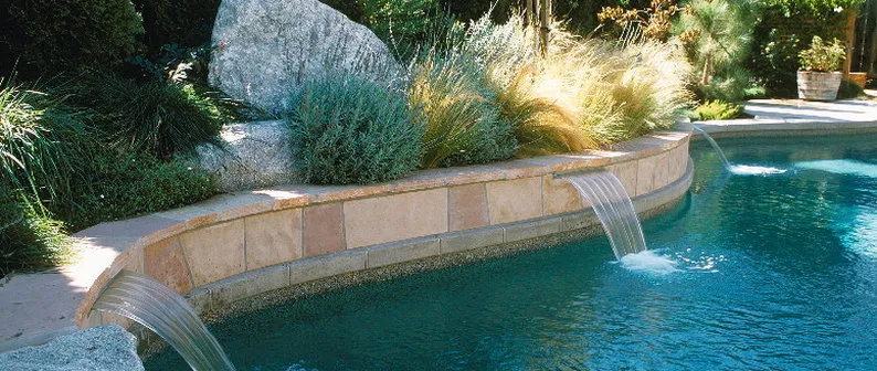 A landscaped poolside area with water features, decorative rocks, and various plants, designed by Confidence Landscaping, Inc. in Campbell.