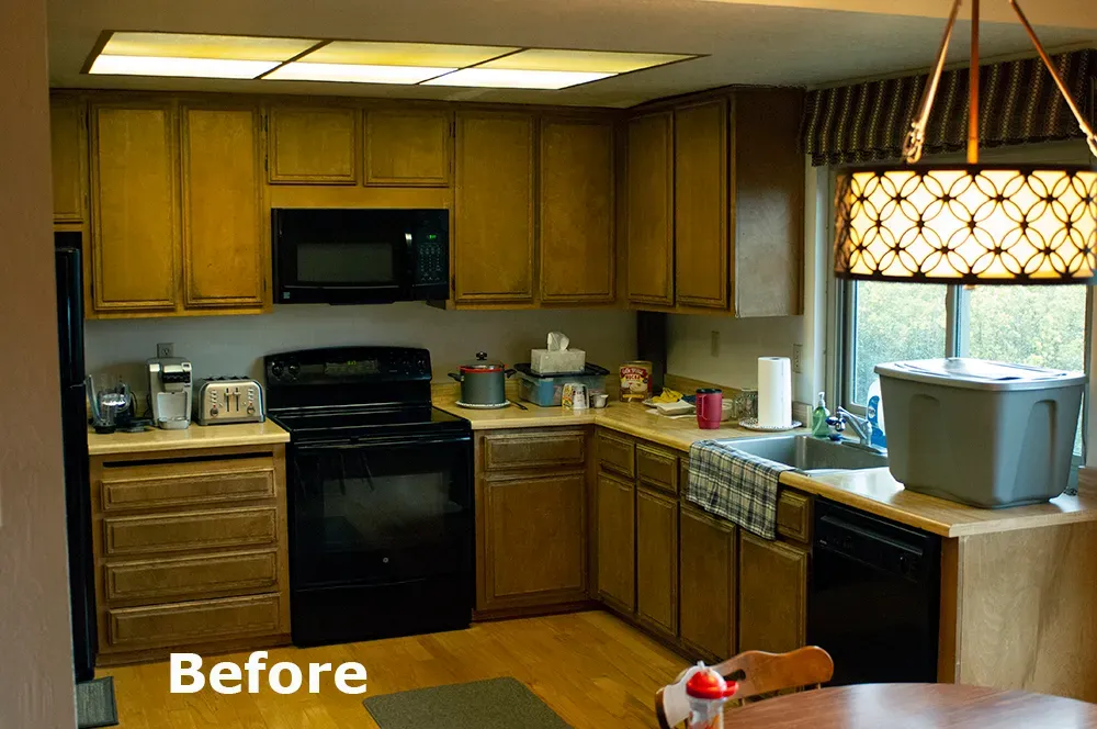 A dated kitchen with wooden cabinets, black appliances, and a large plastic container on the countertop, marked as "Before" for a renovation project.
