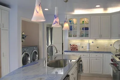 A modern kitchen with white cabinets, blue marble countertops, hanging pendant lights, and adjacent laundry facilities, designed by Cook's Kitchen & Bath, Inc. in Benicia.