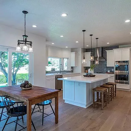 A spacious, modern kitchen with a large island, wooden floor, pendant lights, and a wooden dining table, designed by Craft Builders Construction in Morgan Hill.