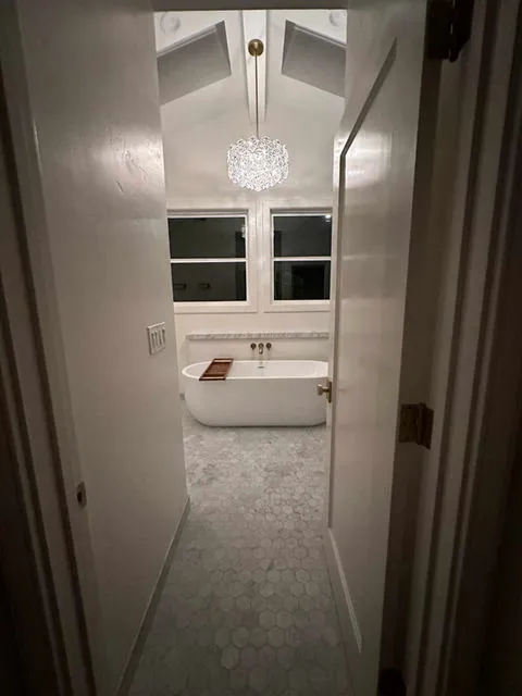 A modern bathroom featuring a freestanding bathtub under a stylish chandelier, designed by Craft Builders Construction in Morgan Hill.