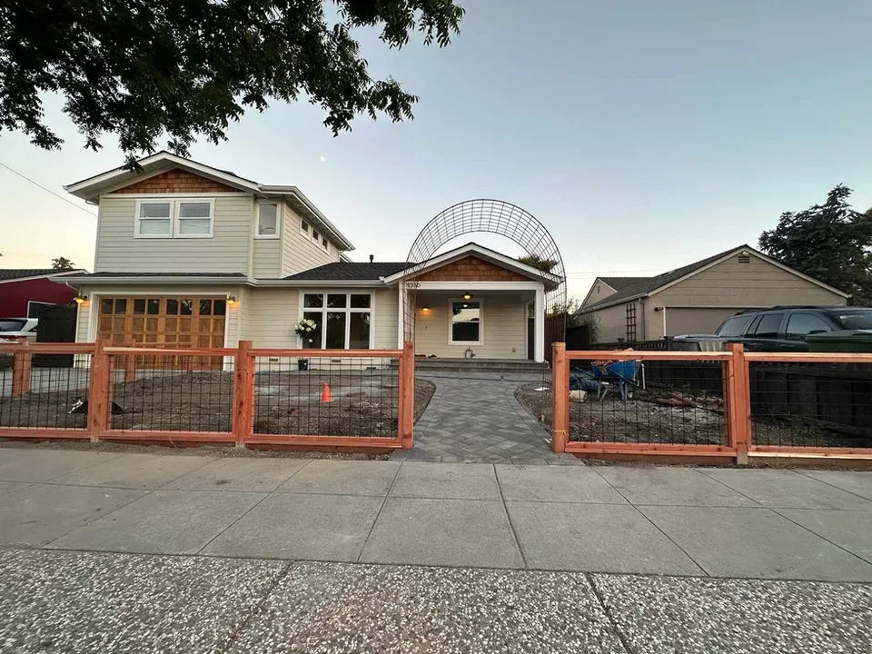 Front view of a two-story house with wooden and light-colored exterior, featuring a wooden fence and driveway, constructed by Craft Builders Construction in Morgan Hill.
