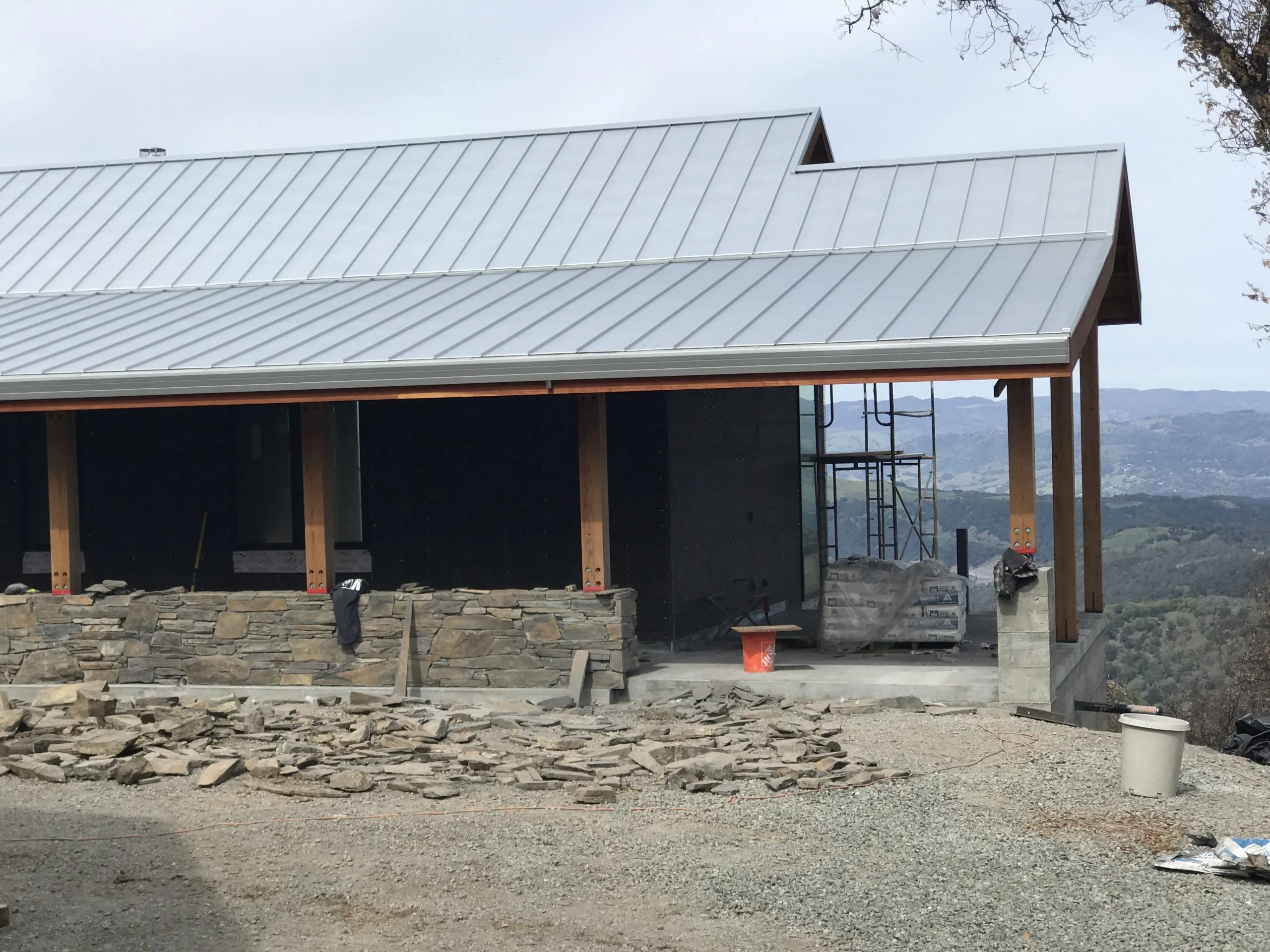 A partially constructed building with metal roofing in Santa Rosa, featuring a stone wall and construction materials, completed by Crandall Roofing Inc.