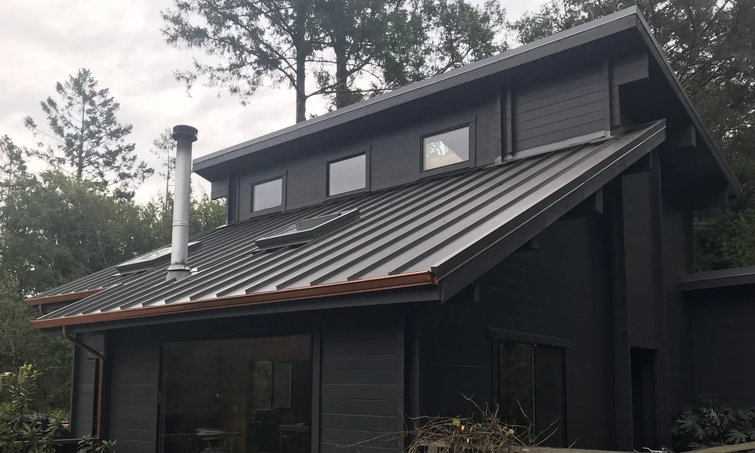 A dark house with a modern metal roof, installed by Crandall Roofing Inc. in Santa Rosa, set against a backdrop of trees.