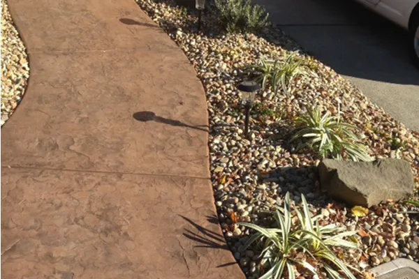 A landscaped walkway in Vacaville, designed by Creative Image Landscaping, featuring a textured pathway bordered by mulch and small green plants.
