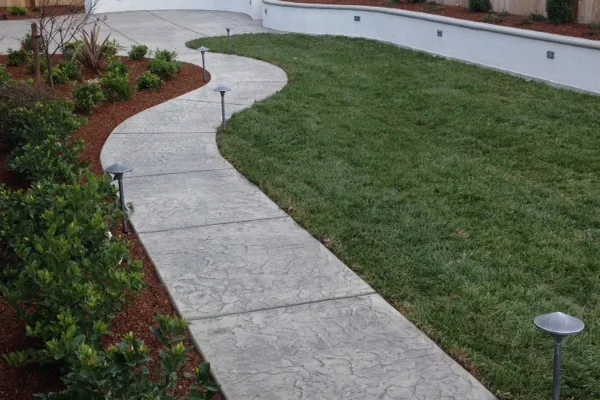 A beautifully landscaped garden featuring a curving concrete path bordered by green grass and neatly arranged shrubs, designed by Creative Image Landscaping in Vacaville.