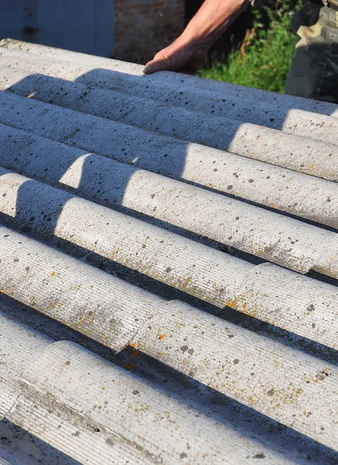 Close-up of hands handling old corrugated asbestos roofing sheets for safe removal.