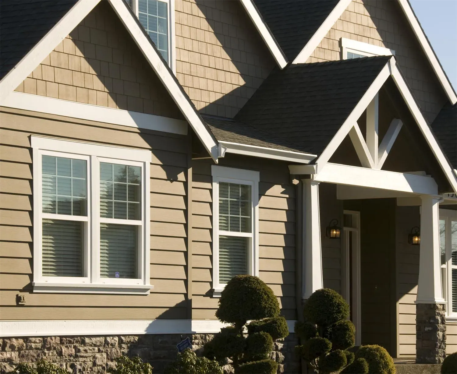 A home exterior showcasing wood siding with stone accents, white-framed windows, and neatly trimmed shrubs, demonstrating the craftsmanship of Custom Exteriors, Inc. in Pleasanton.