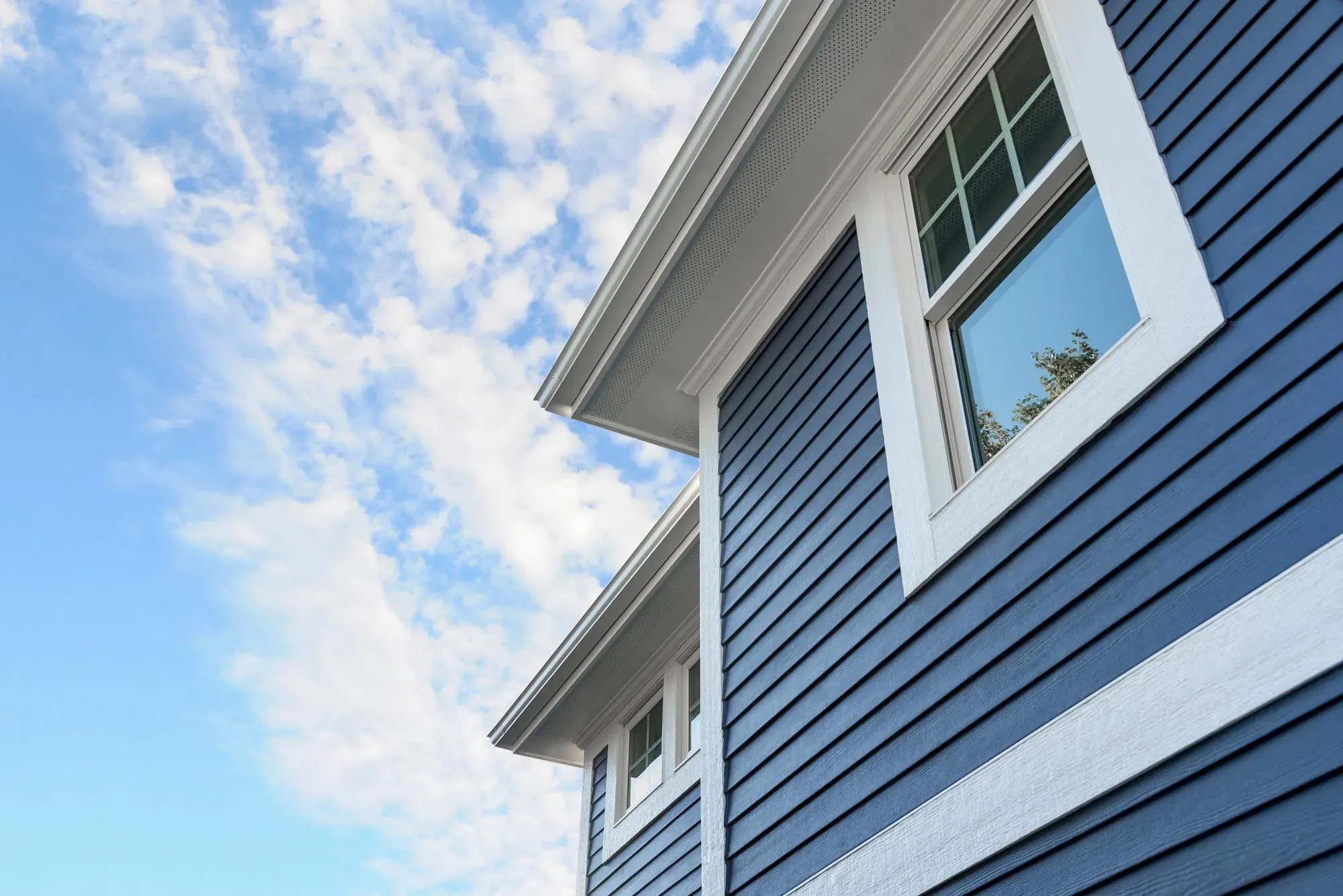 A close-up view of a house with blue siding and white trim, showcasing clean lines and craftsmanship against a blue sky with clouds.