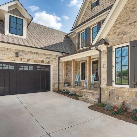 A beautifully designed house exterior in Pleasanton with stone walls, dark shutters, a spacious garage, and a charming front porch with two rocking chairs, showcasing the work of Custom Exteriors, Inc.