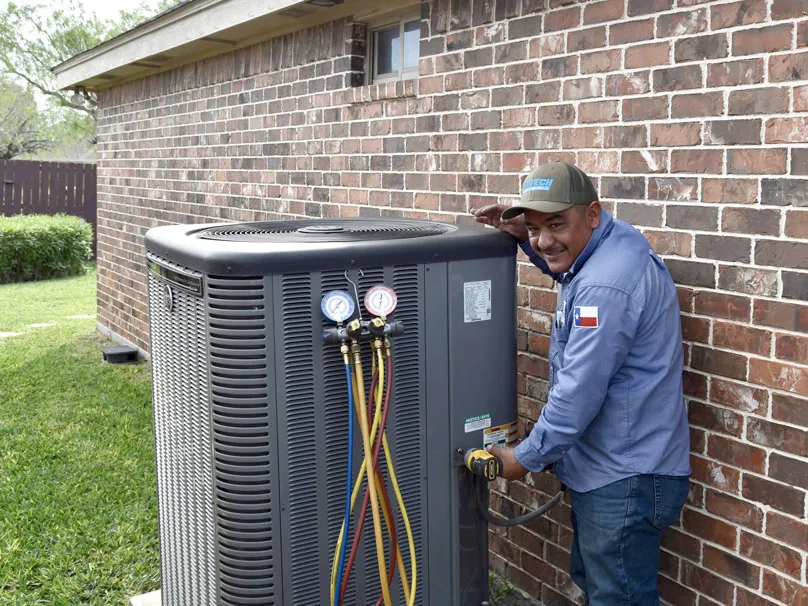 A technician from Cytech Heating & Cooling working on an outdoor air conditioning unit next to a brick house in Edinburg.
