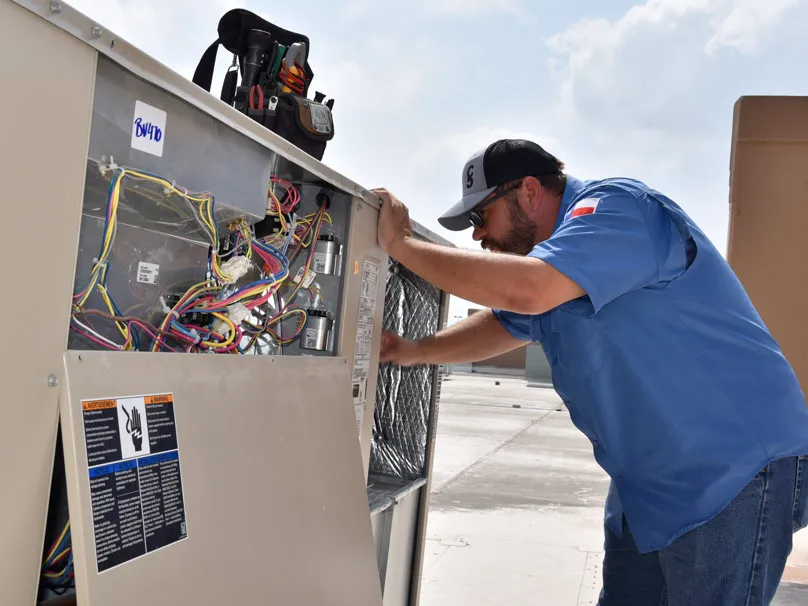 A technician from Cytech Heating & Cooling in Edinburg working on an air conditioning unit, adjusting wiring and components.