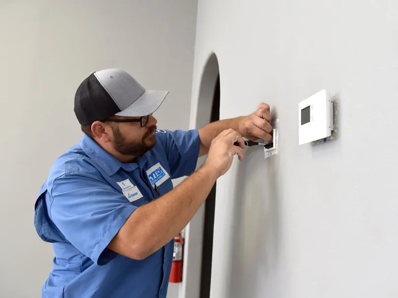 Technician in blue uniform from Cytech Heating & Cooling working on a thermostat installation on a white wall in Edinburg.