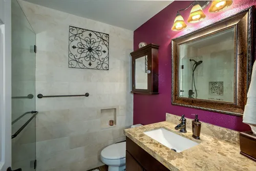 A bathroom featuring a marble countertop, a decorative mirror, a shower with glass doors, and purple accent wall, designed by DC Tile and Stone in Santa Rosa.