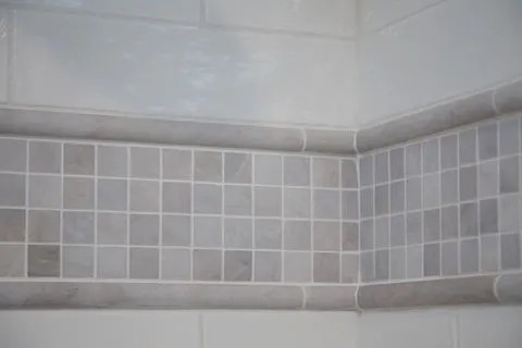 Close-up of a bathroom corner featuring expertly installed square gray tiles bordered by larger rectangular tiles, showcasing D.R. Domenichini Construction's work in Morgan Hill.
