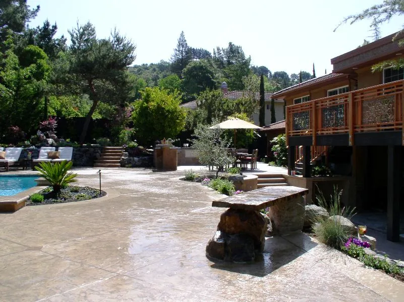 A landscaped outdoor area featuring a pool, seating, plants, and a stone patio designed by Dana Lund Landscaping in San Ramon.