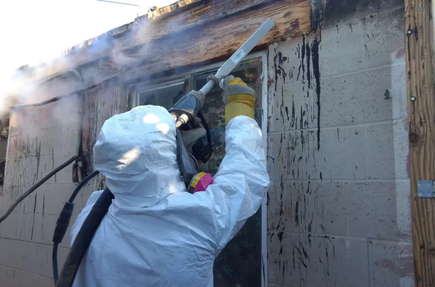 A worker in protective gear from Dansel Restoration Inc. uses equipment to remove mold from a building exterior in San Jose.