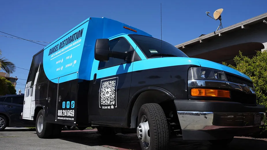 A Dansel Restoration Inc. service van with a blue and black design, parked in a residential area in San Jose.