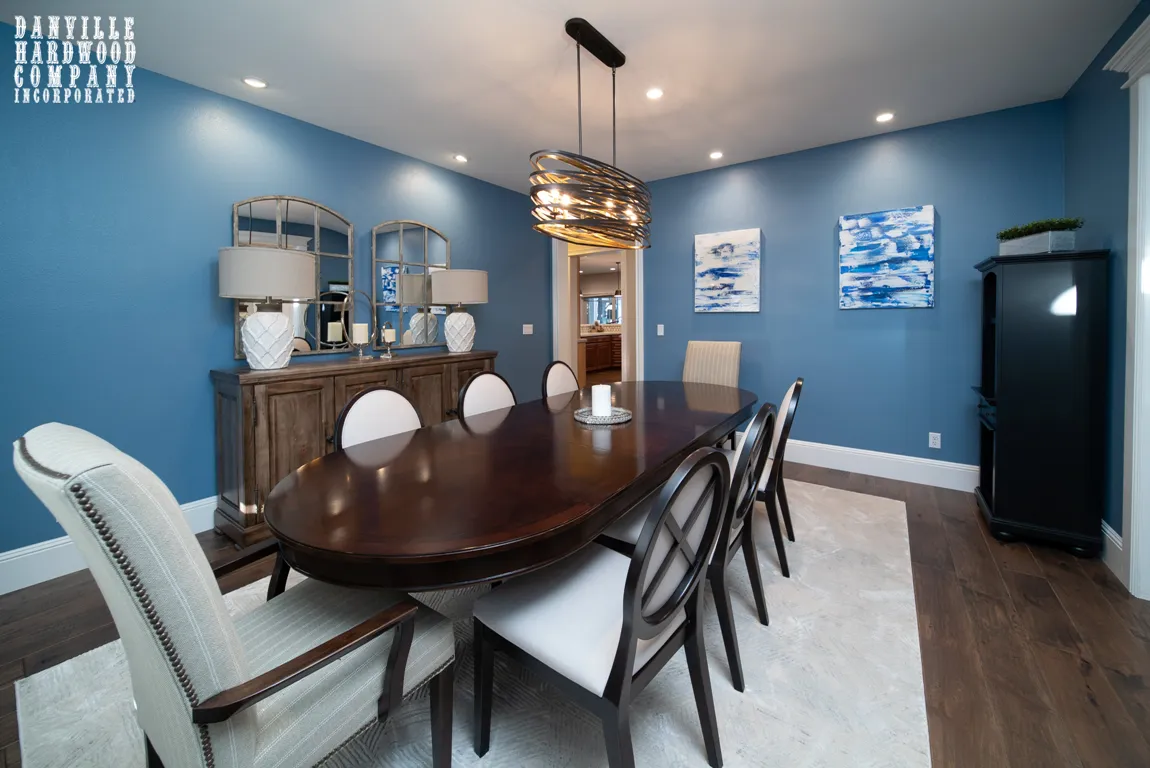 A stylish dining room with a dark wooden table and chairs, blue walls, and hardwood flooring installed by Danville Hardwood Company in Danville.