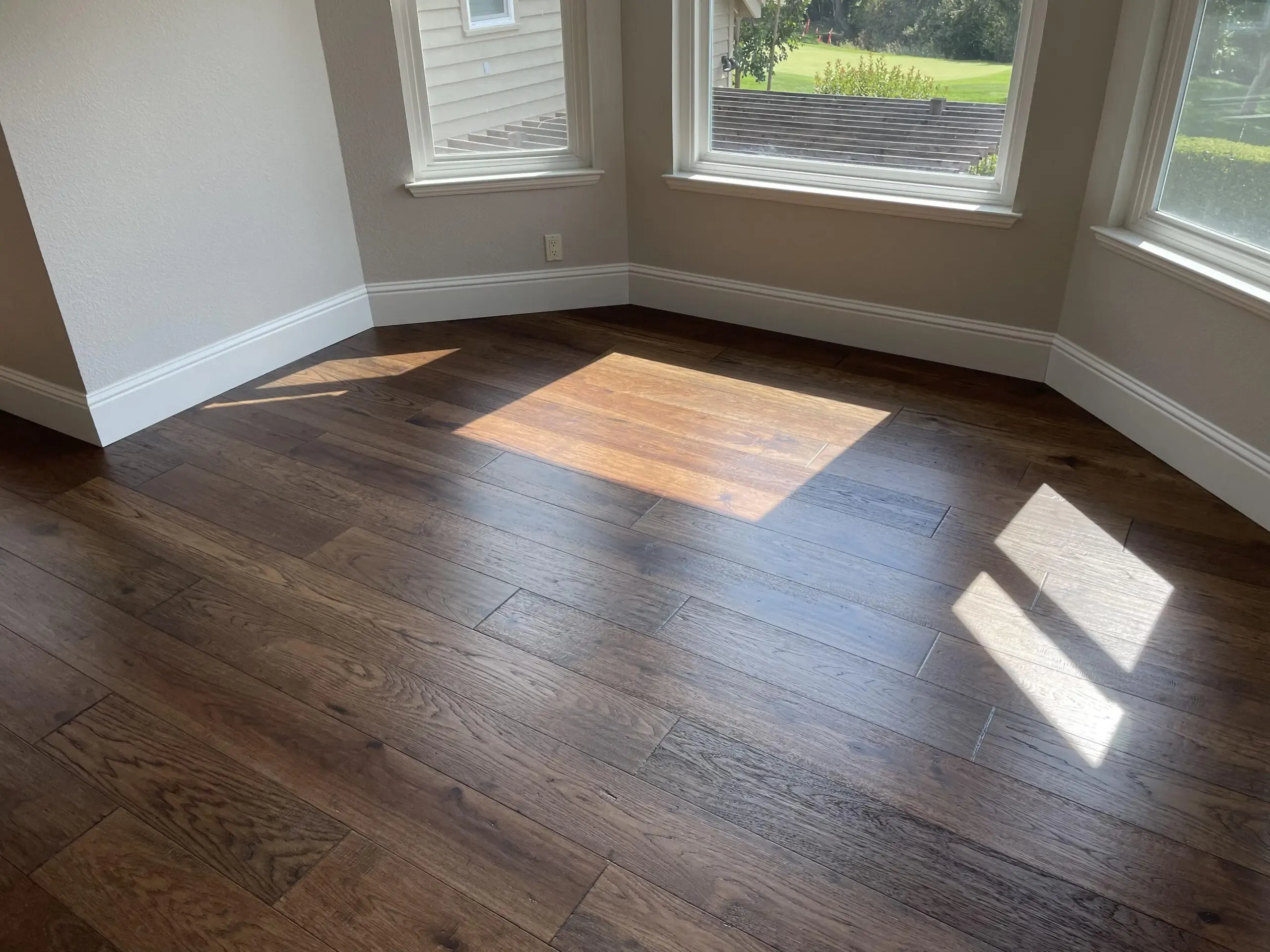 Sunlight streaming onto dark hardwood flooring in a bright room with large windows, installed by Danville Hardwood Company in Danville.