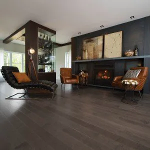 A modern living room featuring dark hardwood flooring by Danville Hardwood Company, with leather chairs, a fireplace, and contemporary decor.