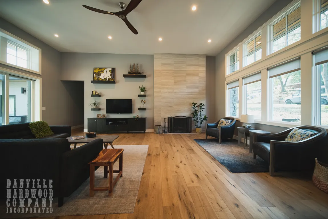A modern living room featuring hardwood flooring by Danville Hardwood Company, with a cozy seating area, large windows, and a contemporary fireplace in Danville.