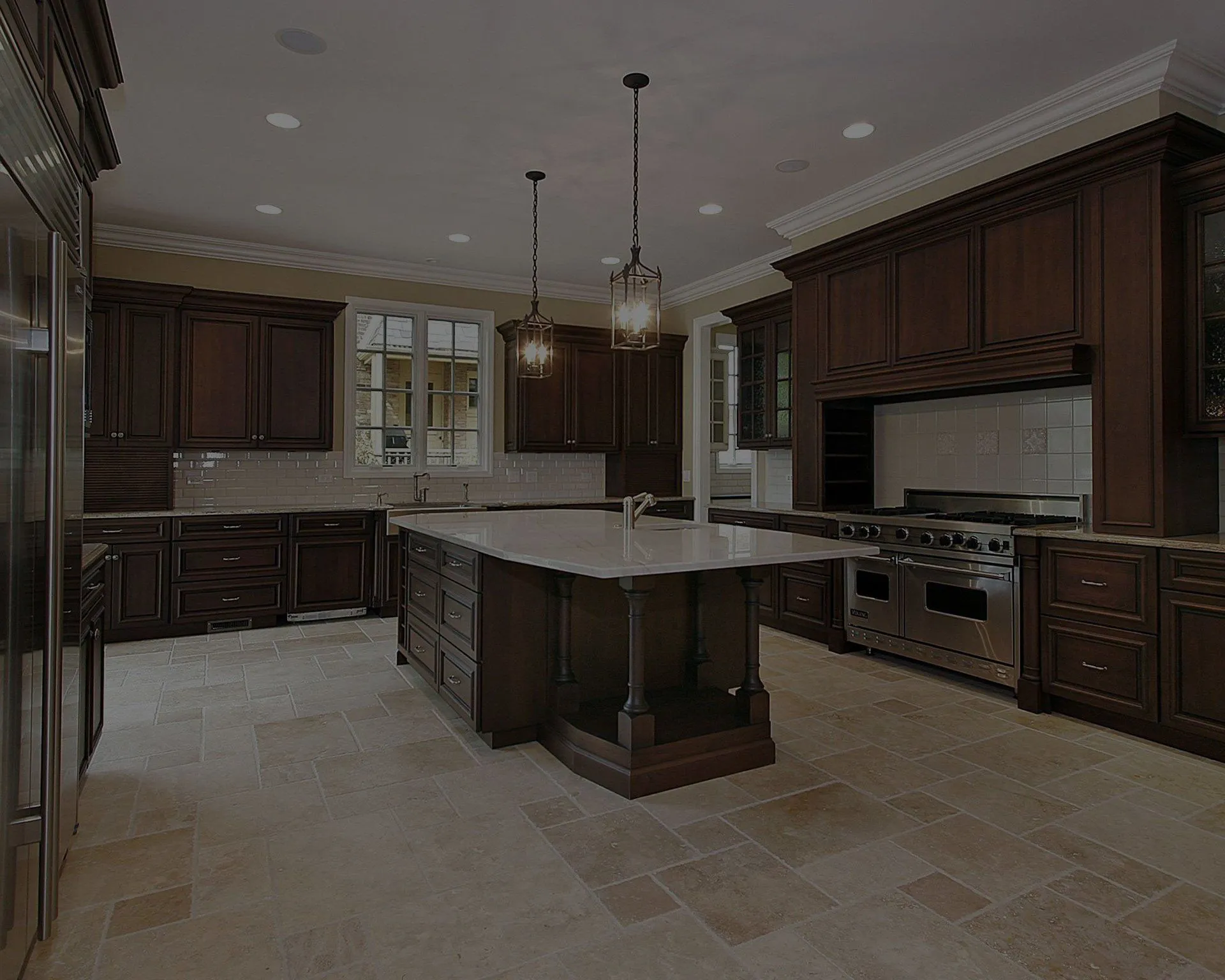 A spacious and modern kitchen with dark wood cabinets, a large center island with a marble countertop, pendant lighting, and stainless steel appliances.