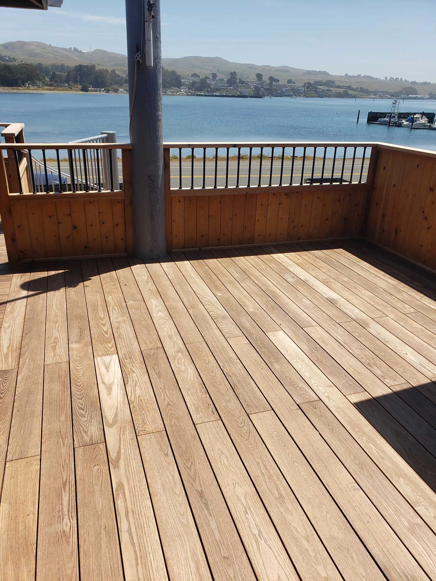 A wooden deck overlooking a serene body of water, built by Deckmaster Fine Decks, Inc. in Sebastopol, displaying precise craftsmanship and natural beauty.