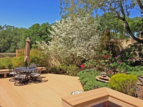 A beautifully crafted wooden deck featuring outdoor seating and surrounded by lush greenery, designed by Deckmaster Fine Decks, Inc. in Sebastopol.