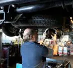 A mechanic working under a vehicle at Delta Transmission in Antioch, focusing on a repair task in a workshop setting.