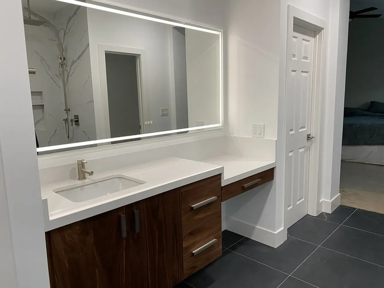 Modern bathroom featuring a large illuminated mirror, white countertop with a sink, and wooden cabinets, designed by Design Miter Tile in Campbell.