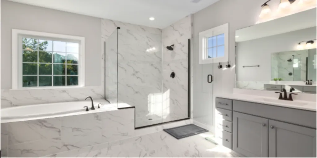 A modern bathroom featuring marble tiles throughout, with a bathtub, glass shower enclosure, and a vanity with a large mirror.